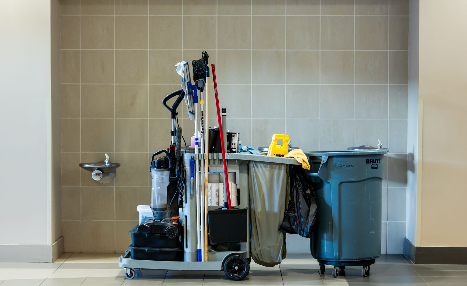 Janitorial cleaning cart with mops, a vacuum and waste bins in a facility corridor