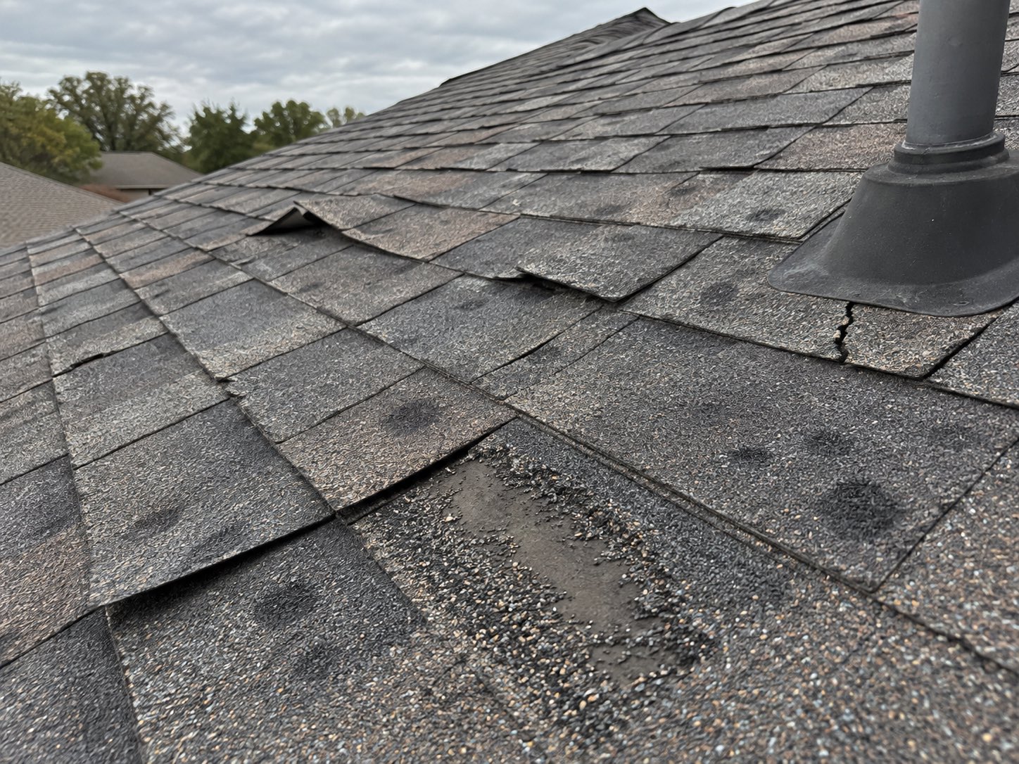 Asphalt shingles with hail damage, lifted tabs and missing granules, photographed at a roof inspection before any work starts